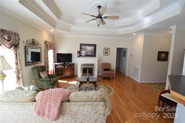 living room with a fireplace, a raised ceiling, a ceiling fan, and light wood-style floors