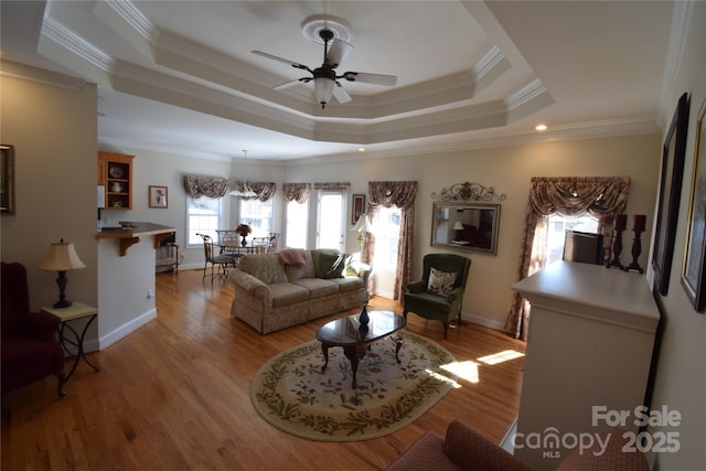 living area with light wood finished floors, a raised ceiling, and crown molding