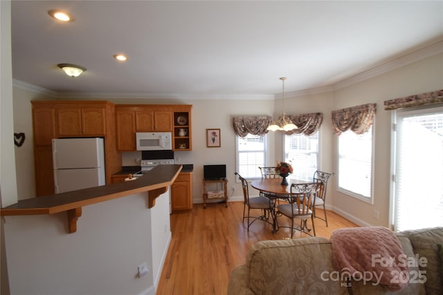 kitchen featuring light wood-style flooring, white appliances, a kitchen breakfast bar, dark countertops, and crown molding