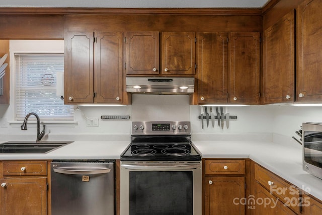 kitchen with appliances with stainless steel finishes, brown cabinets, light countertops, under cabinet range hood, and a sink