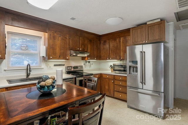 kitchen featuring under cabinet range hood, appliances with stainless steel finishes, light countertops, and a sink