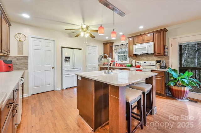 kitchen featuring brown cabinetry, white appliances, light countertops, and an island with sink