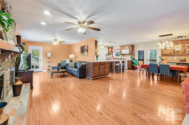 living room with light wood finished floors, ceiling fan, a stone fireplace, french doors, and recessed lighting