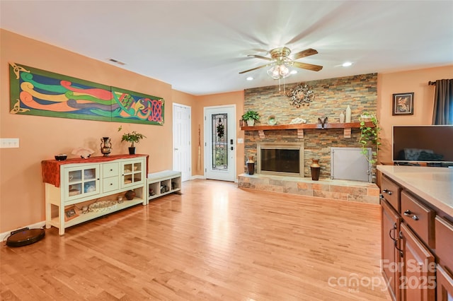 living room featuring ceiling fan, light wood-type flooring, a fireplace, and visible vents