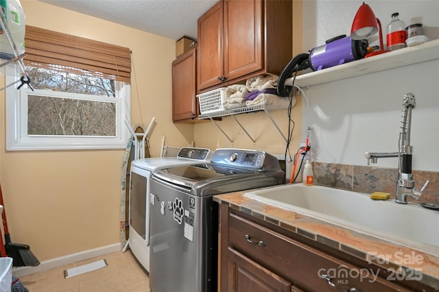 washroom with cabinet space, light tile patterned flooring, a sink, a textured ceiling, and independent washer and dryer