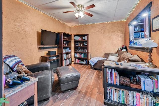 sitting room with a ceiling fan, wood finish floors, a textured wall, and a paneled ceiling