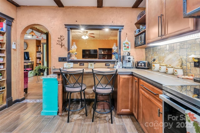 interior space with arched walkways, stainless steel range with electric cooktop, beam ceiling, decorative backsplash, and wood tiled floor