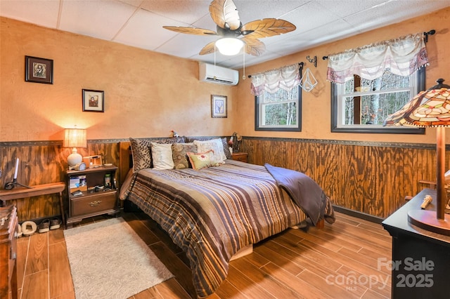 bedroom featuring a wainscoted wall, wood finish floors, a wall mounted AC, and wooden walls