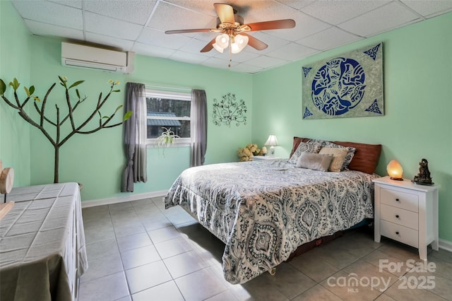 bedroom with light tile patterned floors, baseboards, ceiling fan, an AC wall unit, and a paneled ceiling