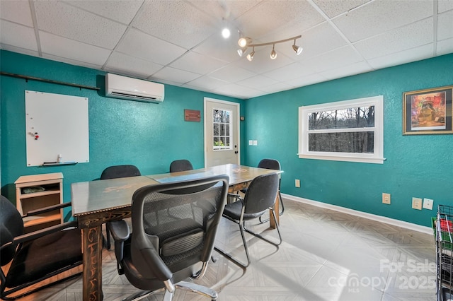 office space featuring a textured wall, a drop ceiling, a wall unit AC, and baseboards