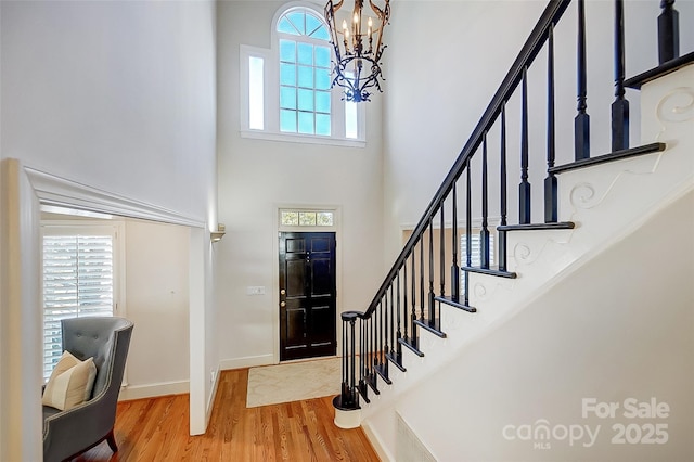 foyer featuring wood finished floors, a towering ceiling, baseboards, stairway, and an inviting chandelier