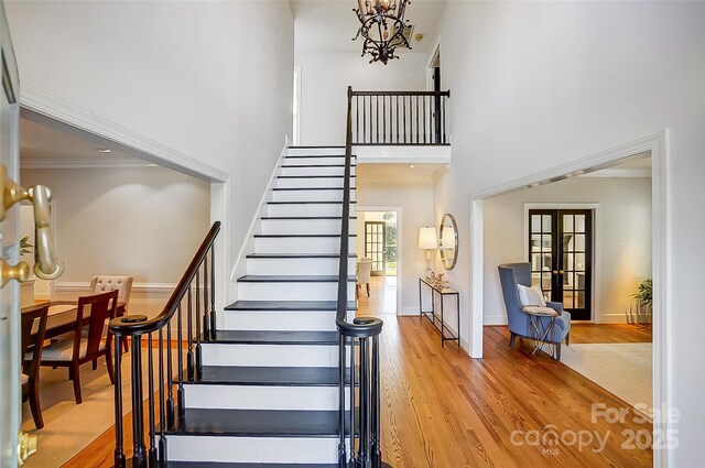 staircase with a high ceiling, ornamental molding, wood finished floors, and french doors