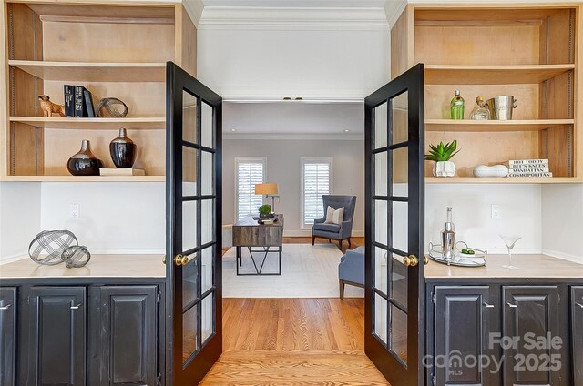 hallway with light wood-style floors, french doors, crown molding, and built in shelves