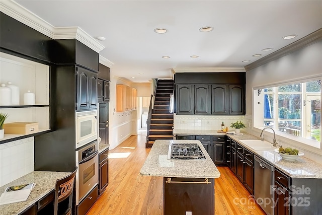 kitchen with light wood-style flooring, ornamental molding, a center island, stainless steel appliances, and a sink