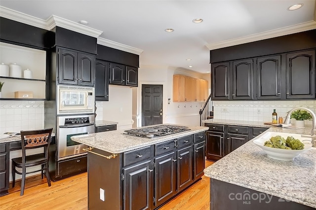 kitchen with dark cabinets, stainless steel appliances, a kitchen island, a sink, and light wood finished floors