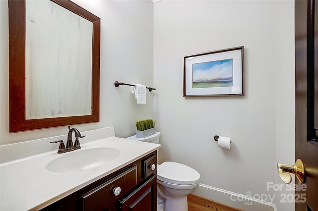 half bathroom with vanity, toilet, and baseboards