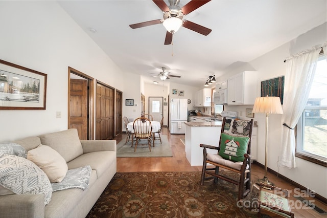 living area featuring lofted ceiling, light wood-type flooring, and baseboards