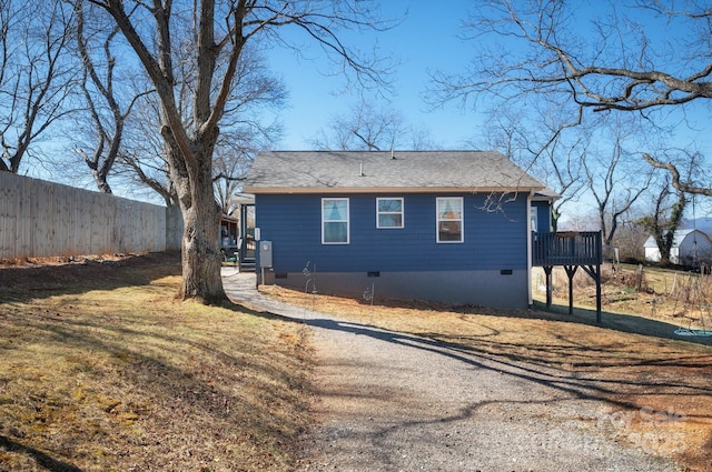 view of side of property with crawl space, fence, and roof with shingles