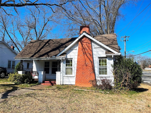 back of property featuring covered porch, a chimney, a lawn, and roof with shingles