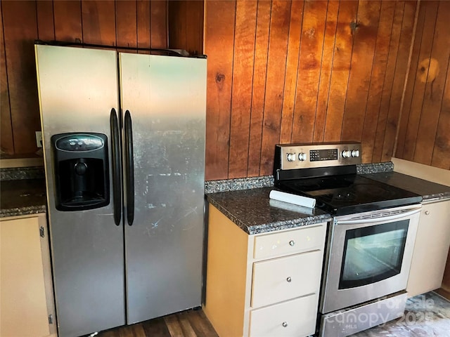 kitchen featuring appliances with stainless steel finishes, dark wood finished floors, wooden walls, and dark stone countertops