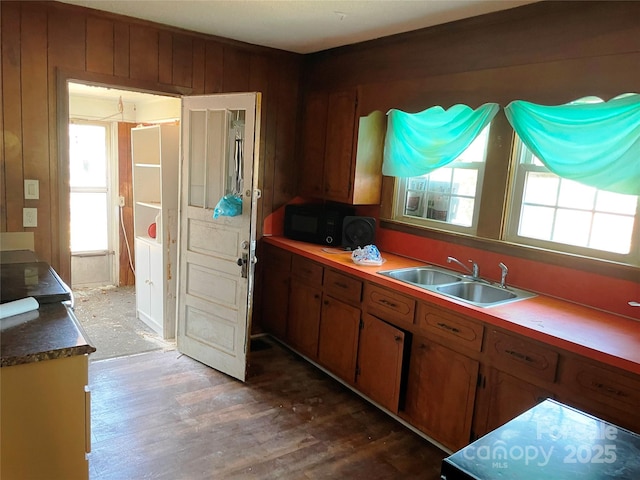 kitchen featuring black microwave, dark wood-style flooring, a sink, brown cabinetry, and dark countertops