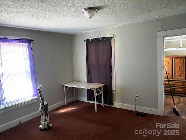 unfurnished bedroom featuring dark colored carpet, multiple windows, a textured ceiling, and baseboards