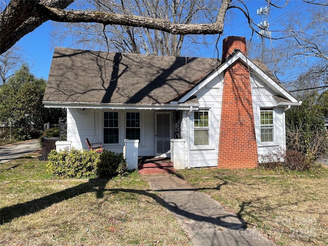 view of front of home with a shingled roof, a chimney, a porch, and a front yard