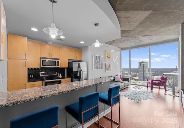 kitchen featuring a breakfast bar, floor to ceiling windows, stainless steel appliances, wood finished floors, and dark stone counters