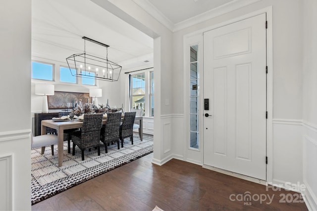 entryway with a decorative wall, a wainscoted wall, crown molding, dark wood finished floors, and an inviting chandelier