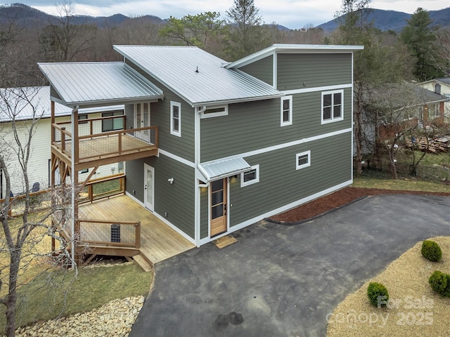 exterior space with a deck with mountain view, metal roof, and aphalt driveway