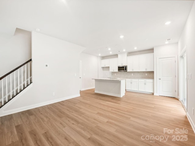 kitchen featuring tasteful backsplash, light countertops, stainless steel microwave, light wood-style flooring, and white cabinetry