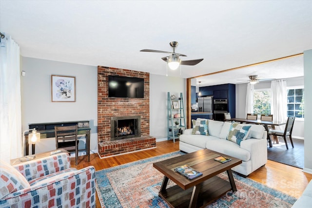 living room with light wood-style floors, ceiling fan, a fireplace, and baseboards