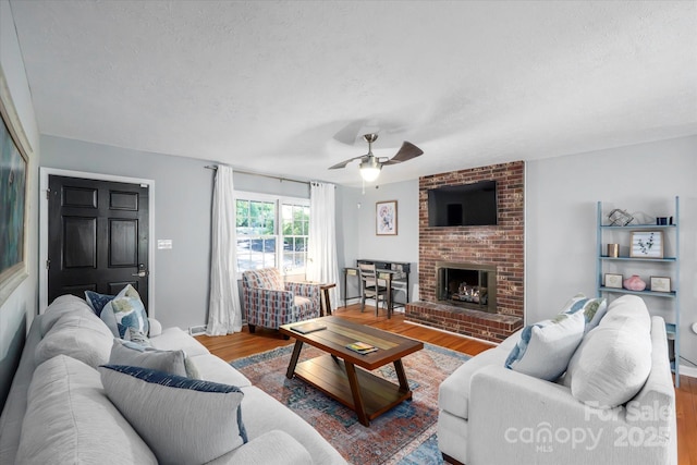 living room featuring a brick fireplace, a textured ceiling, a ceiling fan, and wood finished floors