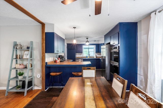 kitchen with a peninsula, blue cabinets, stainless steel appliances, a kitchen bar, and wooden counters