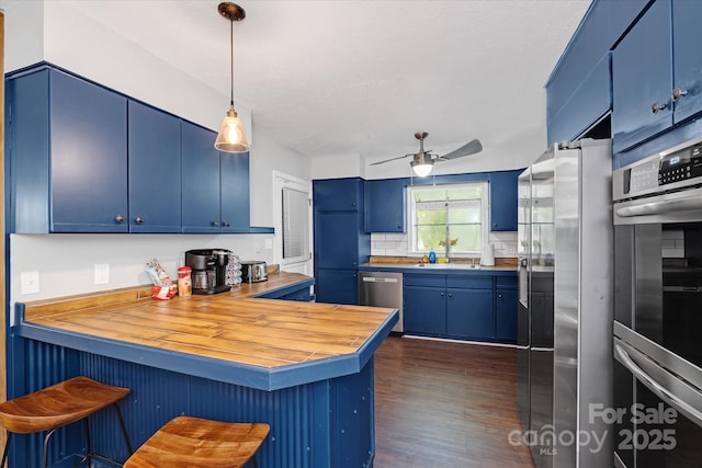 kitchen featuring decorative light fixtures, appliances with stainless steel finishes, blue cabinets, a peninsula, and a kitchen breakfast bar