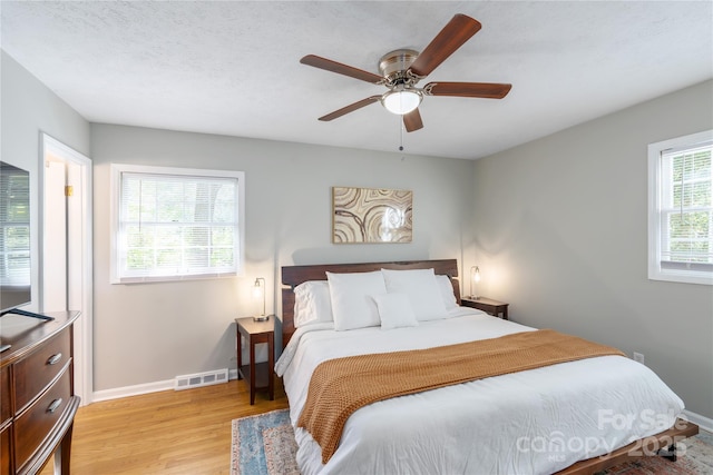 bedroom with light wood-style floors, baseboards, visible vents, and a ceiling fan