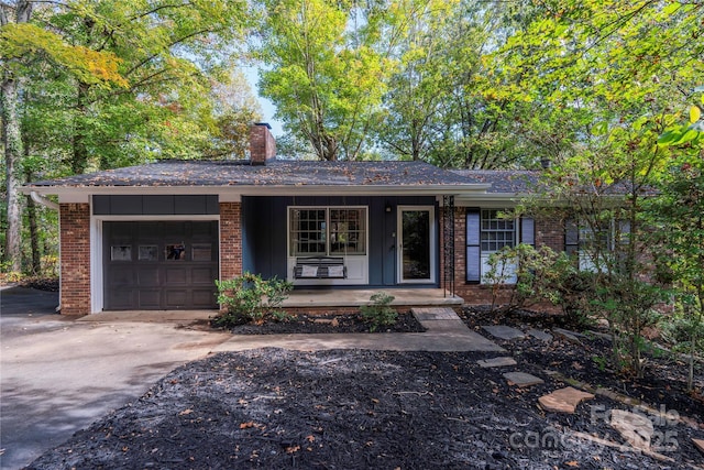 ranch-style home with brick siding, a chimney, covered porch, an attached garage, and driveway