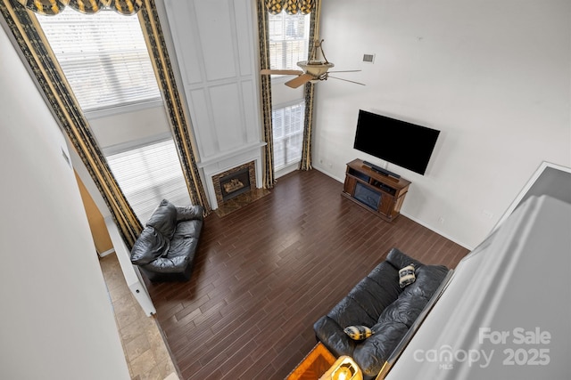 living area with plenty of natural light, a fireplace with flush hearth, ceiling fan, and wood finished floors