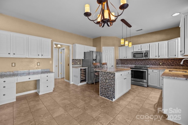 kitchen with decorative backsplash, built in study area, stainless steel appliances, white cabinetry, and a sink