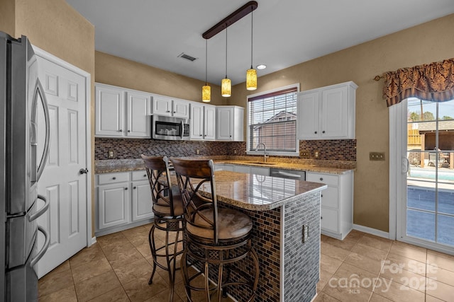 kitchen with stainless steel appliances, visible vents, decorative backsplash, white cabinets, and a sink