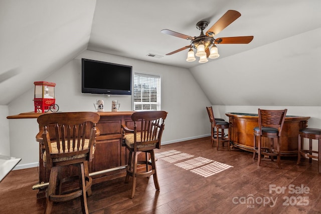 bar featuring visible vents, vaulted ceiling, a bar, wood finished floors, and baseboards