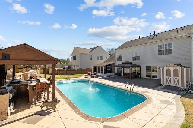 view of swimming pool featuring a fenced backyard, a storage shed, a fireplace, a sunroom, and a gazebo