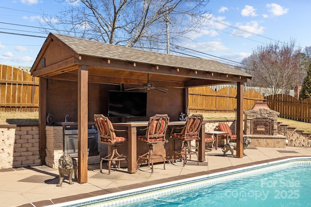 view of swimming pool with a fenced in pool, a patio, a fenced backyard, outdoor dry bar, and an outdoor stone fireplace