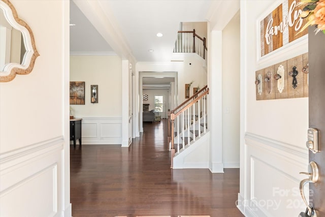 foyer with stairs, ornamental molding, dark wood-type flooring, and a decorative wall