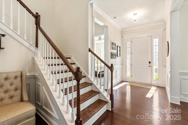 entrance foyer featuring dark wood finished floors, wainscoting, stairway, ornamental molding, and a decorative wall