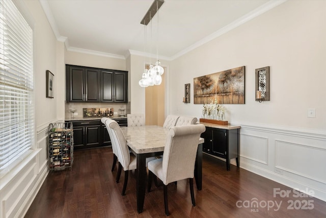 dining room with ornamental molding, dark wood-style flooring, wainscoting, and a decorative wall