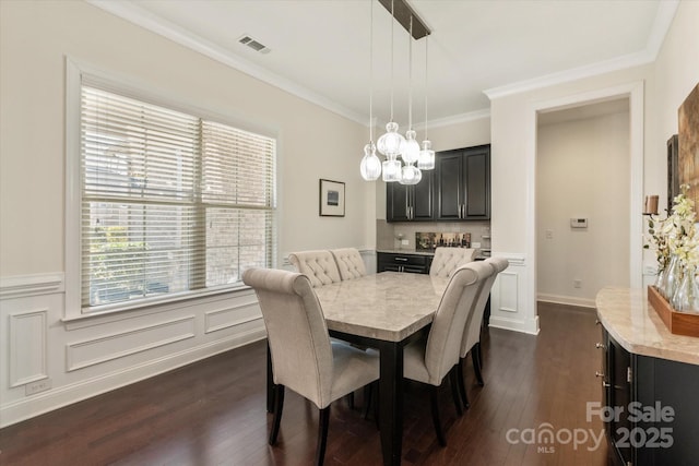 dining space featuring visible vents, dark wood finished floors, a wainscoted wall, crown molding, and a decorative wall