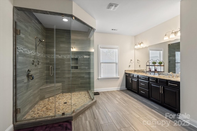 full bathroom with double vanity, a shower stall, visible vents, and baseboards