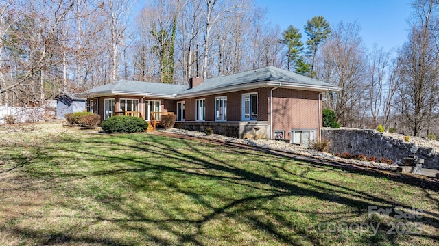 rear view of house with brick siding, a lawn, and a chimney