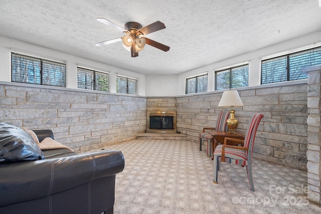 living area featuring plenty of natural light, a fireplace, a ceiling fan, and a textured ceiling